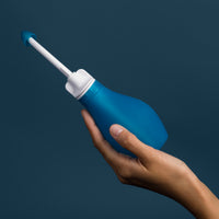 RhinoRinser blue sinus rinse bottle held in hand on a dark blue background